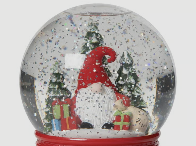 En snöglob med tomte, paket och granar och snö yrande omkring.